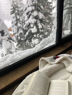 an open book sitting on top of a white blanket next to a snow covered tree