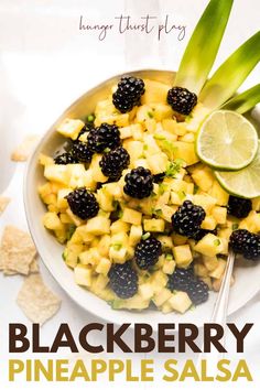 a white bowl filled with pineapple salsa and topped with blackberries next to a lime wedge