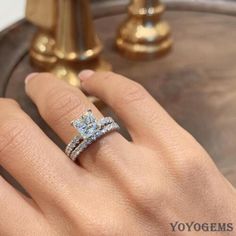 a woman's hand with a diamond ring on top of her finger, next to a gold pedestal