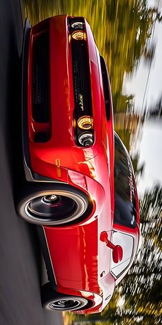 the rear end of a red sports car driving down a road with trees in the background