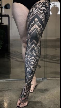 a woman with black and white tattoos on her leg, standing in front of a mirror