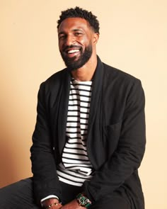 a man sitting on top of a wooden chair wearing a striped shirt and black jacket