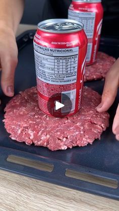 two cans of soda being put on top of hamburger patties