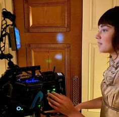 a woman standing in front of a wooden door holding a remote control device and looking at it