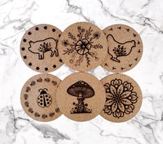 four cork coasters with designs on them sitting on a marble countertop next to flowers and ladybugs