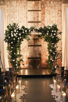 an aisle decorated with white flowers and greenery for a wedding ceremony in front of a brick wall