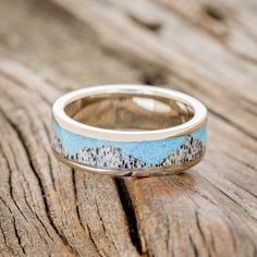 a wedding band that has mountains painted on it and is sitting on a wooden surface