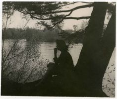 an old photo of a woman sitting on a tree by the river talking on her cell phone