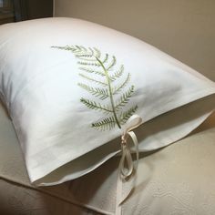 a white pillow with a green fern embroidered on the front and side, tied to a bed frame