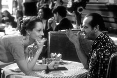 a man and woman sitting at a table in a restaurant talking to each other while eating food