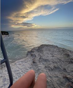 someone is sitting on the beach watching the sun rise over the water and clouds in the sky