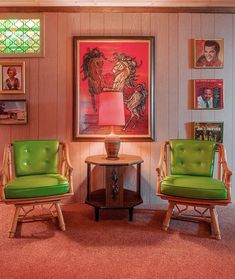 two green chairs and a table in a room with pictures on the wall behind them