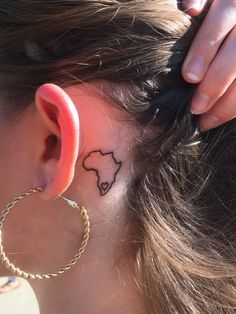 a woman with a small tattoo on her left side behind the ear is wearing a gold hoop