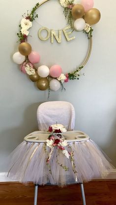 a chair with a tutu and balloons attached to the back of it, sitting in front of a wall that says one