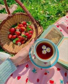 a person is holding a basket with strawberries in it next to a cup of tea