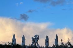 a group of statues sitting on top of a lush green hillside under a cloudy blue sky