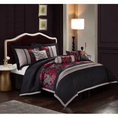 a bed with black and red comforters in a room next to a lamp on a table