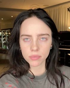 a woman with long black hair and blue eyes is looking at the camera while wearing a gray t - shirt