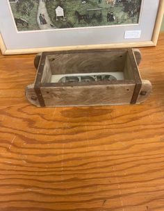 a wooden box sitting on top of a wooden table next to a framed painting with horses in the background