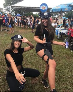 two women dressed in police uniforms sitting on the ground at an outdoor music festival with people standing around