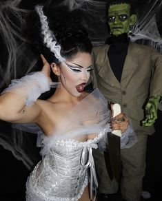 a woman dressed in white holding a knife next to a man with green makeup on his face