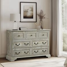 a white dresser with drawers in front of a window next to a painting on the wall