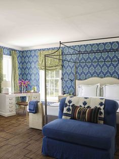 a bedroom decorated in blue and white with a four poster bed, chair, desk, dresser and window