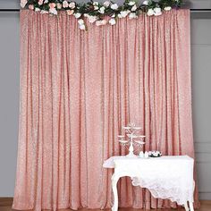 a table with a cake on top of it next to a pink curtain and flowers