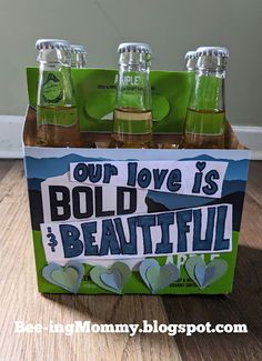 four bottles of soda sitting in a box on top of a wooden table with the words our love is bold and beautiful