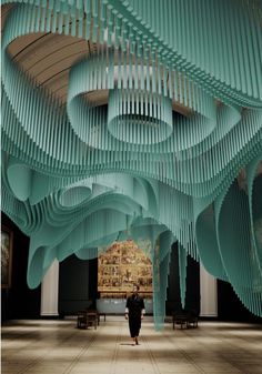 a woman walking through a large room with lots of blue pipes hanging from the ceiling