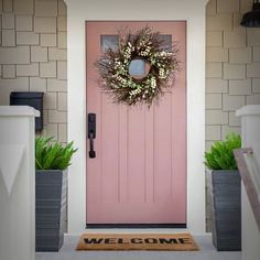 a pink front door with two planters and a welcome mat