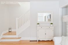 a living room with white furniture and wood flooring in front of a stair case