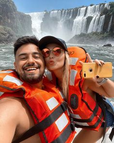 a man and woman taking a selfie on a boat in front of a waterfall