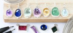 seven different colored glass pendants sitting on top of a wooden board next to scissors