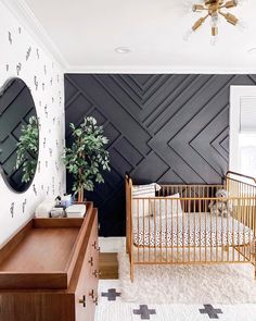 a baby's room with black and white wallpaper, gold crib, wooden dresser, and potted plant