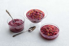 three small bowls filled with food on top of a white tablecloth next to two spoons