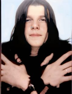 a woman with long black hair and piercing on her nose is looking at the camera