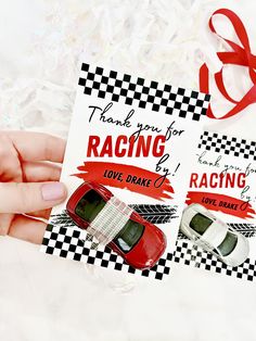 a hand holding a card with two cars on it and a red ribbon around it