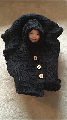 a small child in a black crocheted blanket on the floor with a button