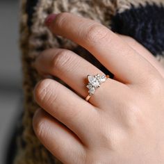 a woman's hand with a diamond ring on her finger, wearing a sweater