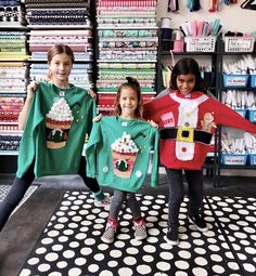 three girls in christmas sweaters holding up cupcakes and santa's helper