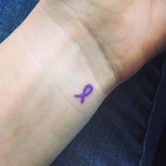 a small purple ribbon tattoo on the wrist