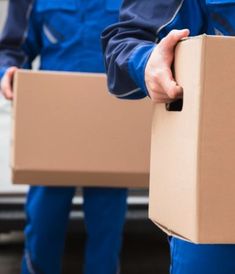 two men in blue overalls holding boxes near a car with the back door open