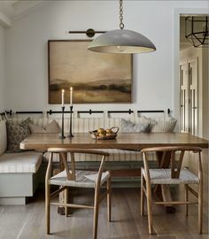 a dining room table with two chairs and a bench in front of it, next to a painting on the wall