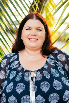 a woman smiling for the camera with palm trees in the backgroung behind her