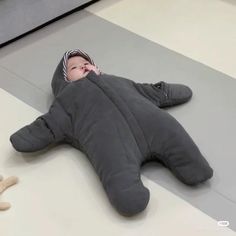 a baby is laying on the floor wearing a sleeping bag with a shark shaped body