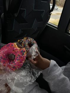 a person holding two doughnuts in their hand while sitting in the back seat