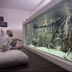 a man sitting on a bean bag chair in front of an aquarium filled with fish