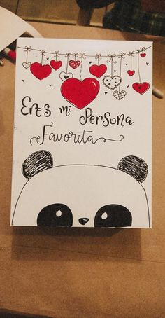 a greeting card with a panda face and hearts hanging from the strings, on top of a table