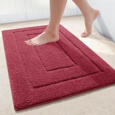 a woman's bare feet are standing on a red rug in front of a window